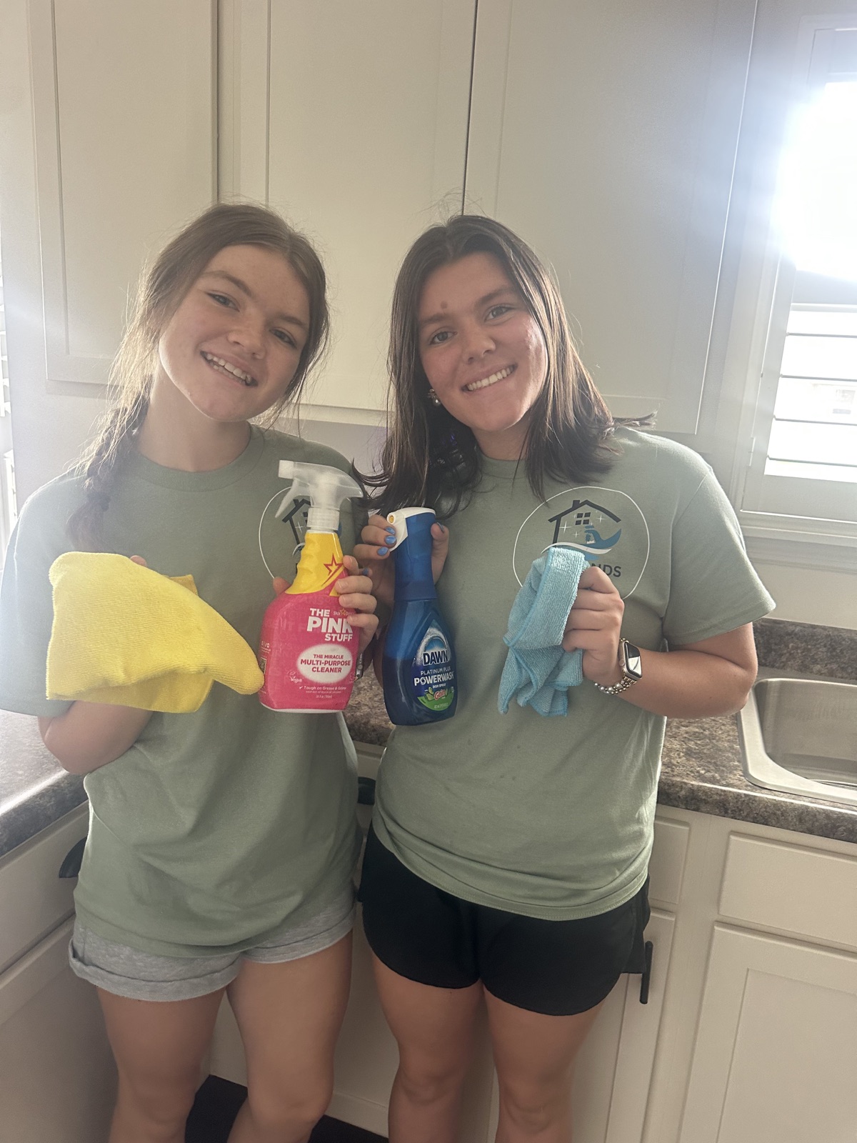 Two All Hands Cleaning team members smiling in uniform with cleaning supplies